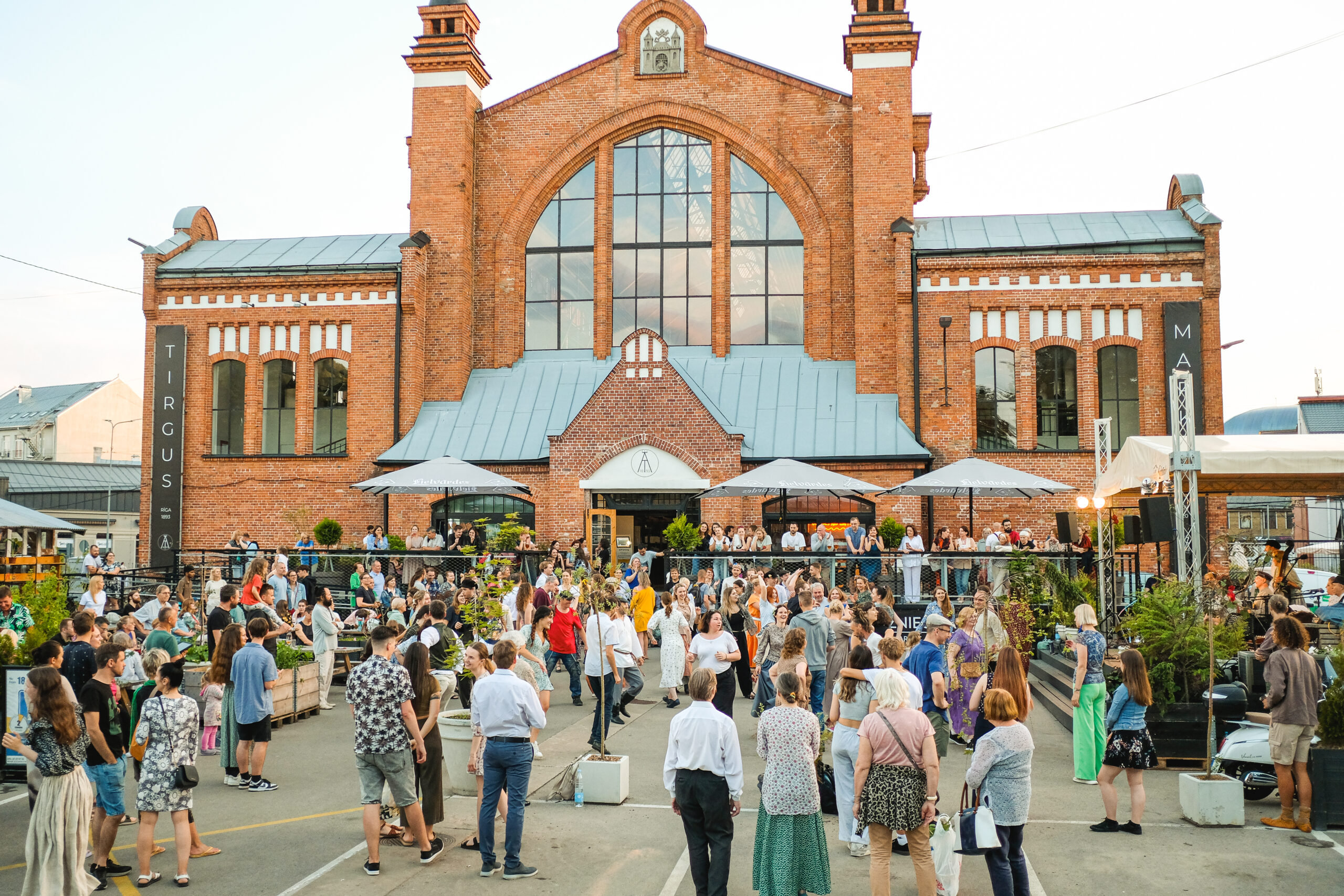 People gathered at Āgenskalns Market, the brick building of Āgenskalns Market is visible in the background